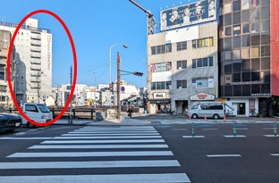 前方右側の横断歩道を渡ってください。橋を挟んで左側にホテルが見えます。